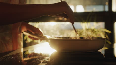 a woman fries vegetables in a frying pan, in the background a window from which the sun shines