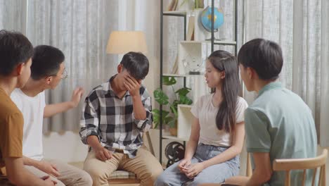 asian teen group sitting in chairs forming a circle discussing at home. teen students support a boy in plaid shirt not to crying