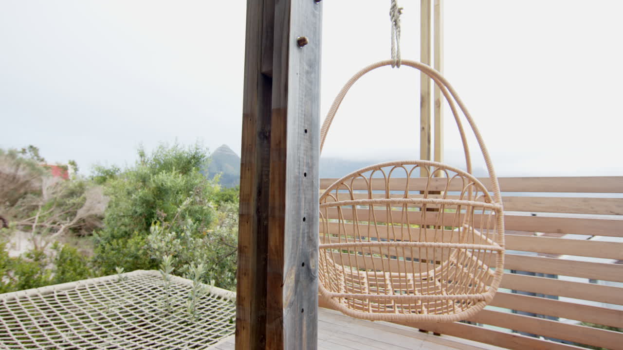 Hanging wicker chair on cozy porch overlooking lush green landscape, copy space