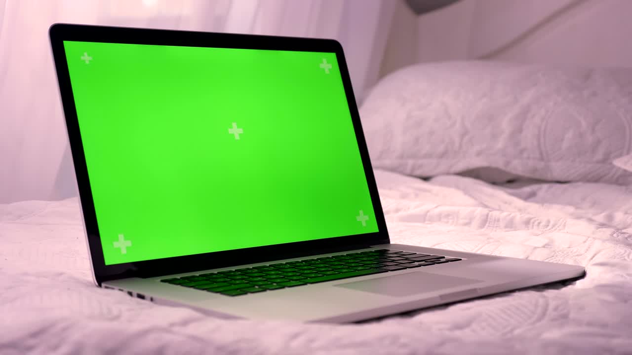 Closeup shoot of laptop with green chroma-key screen laying on the bed. Advertisement on the screen