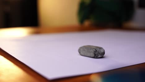 heavily used small eraser is placed on a white paper on a wooden table