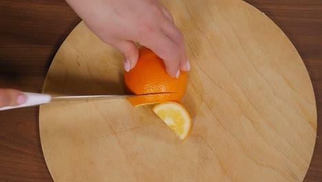 close-up of a woman slicing an orange with a knife on a wooden chopping board.