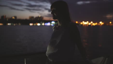 silhouette of a young attractive woman against a background of a night city aboard a boat