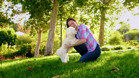 mujer acariciando y abrazando a un perro blanco en el parque