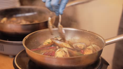 steaming clams cooking with herbs and vegetables in frying pan on stove