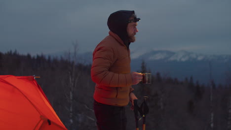 tourist drinking hot tea at campsite in mountains