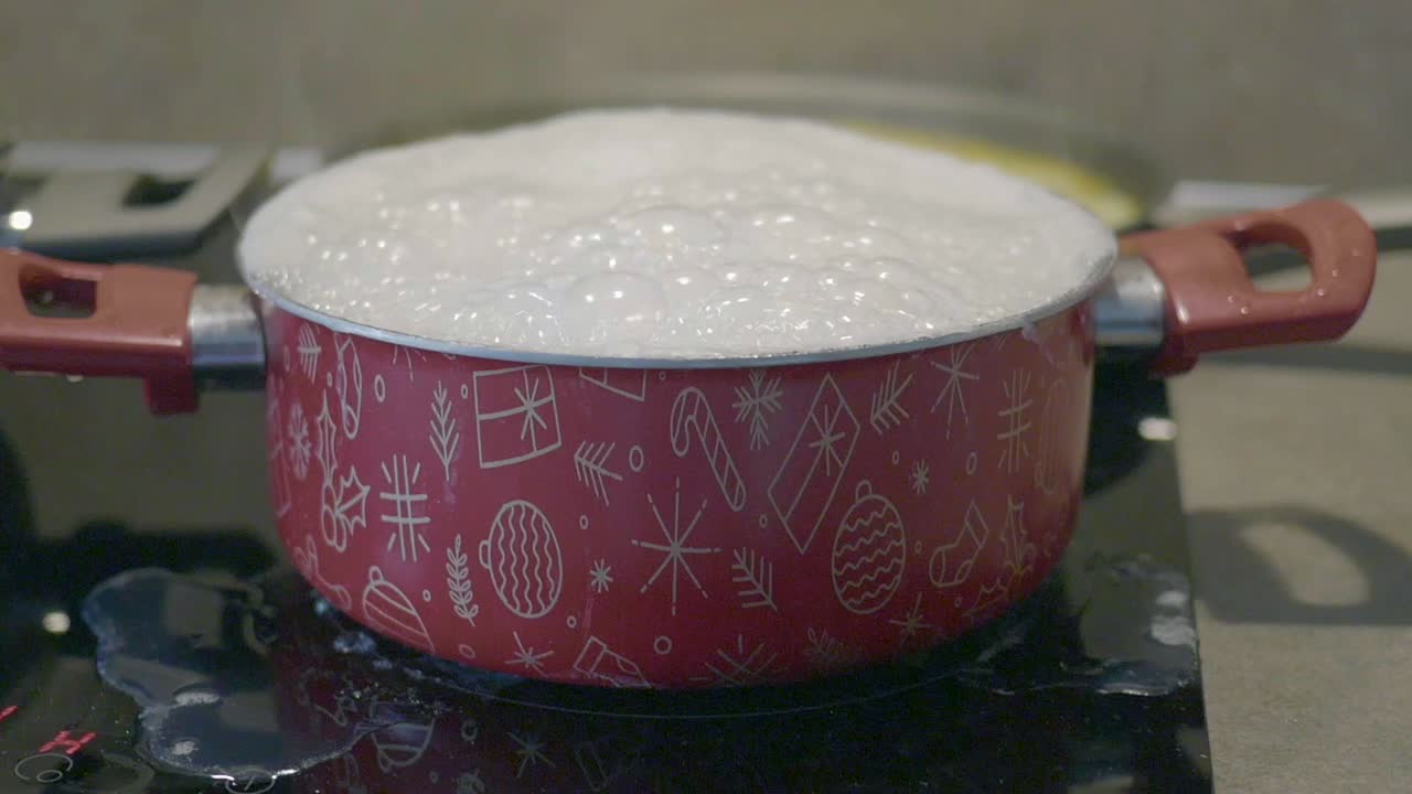 olla roja con diseño de navidad hirviendo agua en la estufa