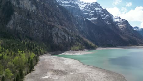 Aerial-forward-view-of-shoreline-of-an-alpine-lake-in-a-fantastic-mountain-landscape