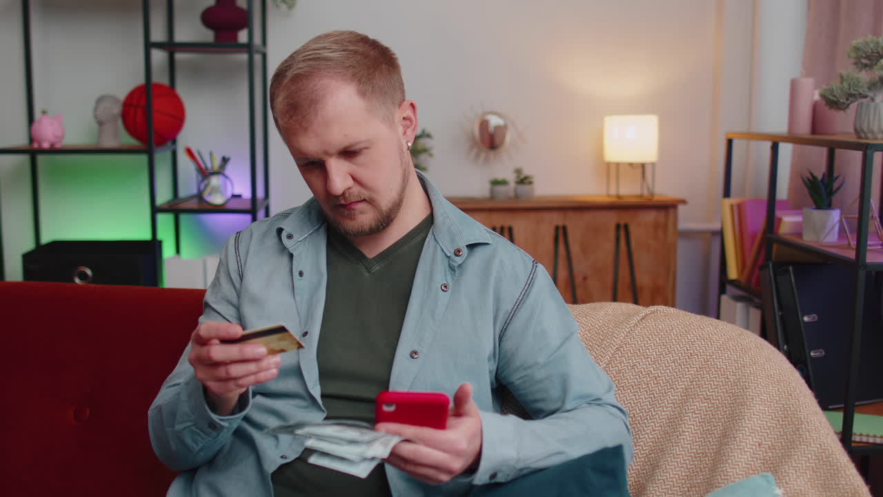 Мужчина сидит дома, используя кредитную банковскую карту и смартфон, переводя деньги в онлайн-покупках