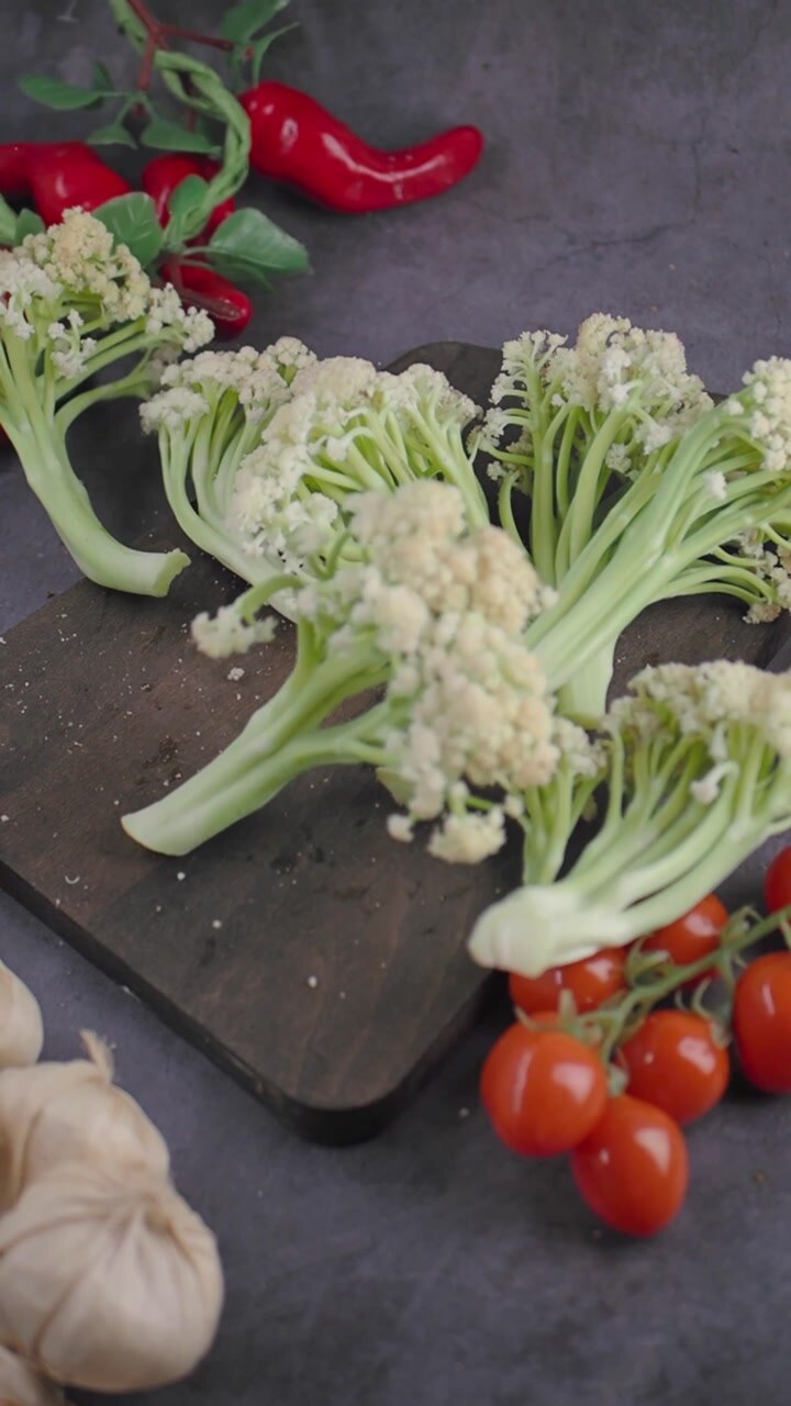 Fresh Cauliflower Florets Dropping onto a Cutting Board with Tomatoes and Garlic