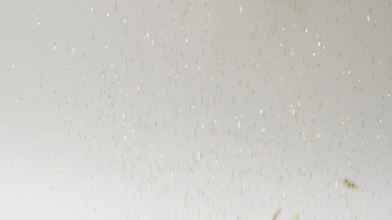 Video of glittering gold confetti falling on white background