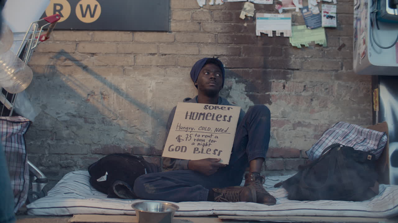 Homeless Man Sitting on Street with Cardboard Sign Asking for Help