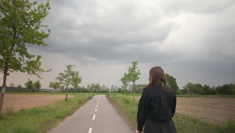 girl in a long black dress walks along a path lined with trees