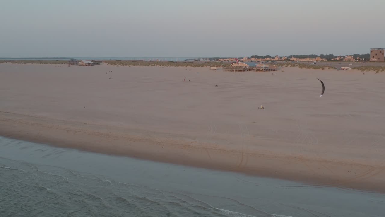 Cinematic drone - aerial panorama circling shot of the green and sandy nature beach with Buggykiting at sunset with tourists and people  at Zeeland at the north sea, Netherlands, 25p