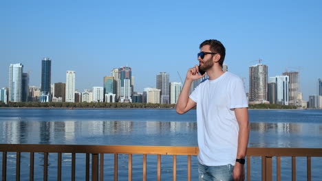 Happy-young-man-walking-on-the-street-and-looking-aside-while-talking-by-his-phone