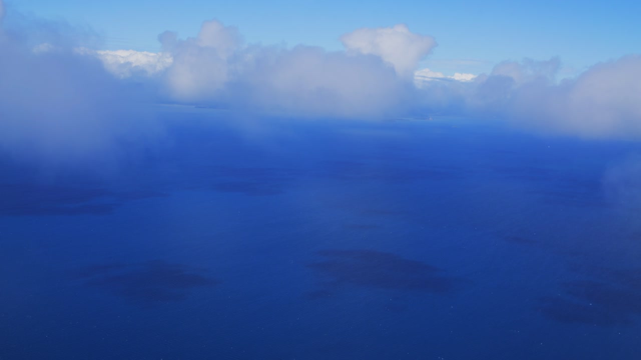 비행기에서 바라보는 바다 위 구름 사이로 숨막히는 광경이 포착되며, 짙푸른 바다와 대비되는 하얀 뭉게구름의 아름다움이 돋보인다.