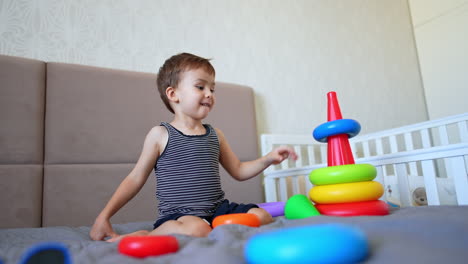 beautiful little kid sits on the bed playing with pyramid. low angle view at the toddler busy with a toy.
