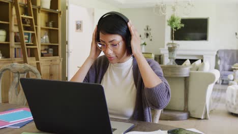 Happy-biracial-teenager-girl-sitting-at-table-and-using-laptop,-in-slow-motion