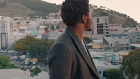 attractive young african american man enjoying rooftop view of city skyline at sunset smiling happy drinking refreshing cold beer celebrating weekend party