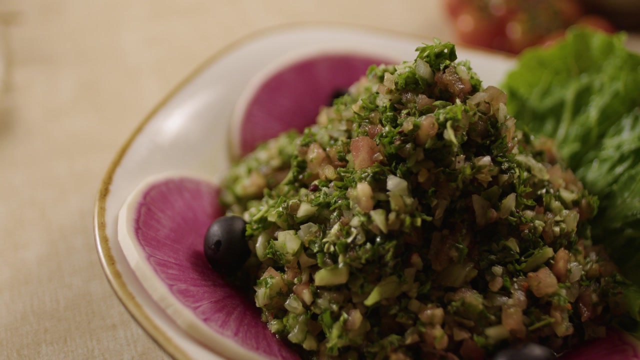 Insalata mista fresca con prezzemolo, pomodori e olive servita su un piatto decorato.