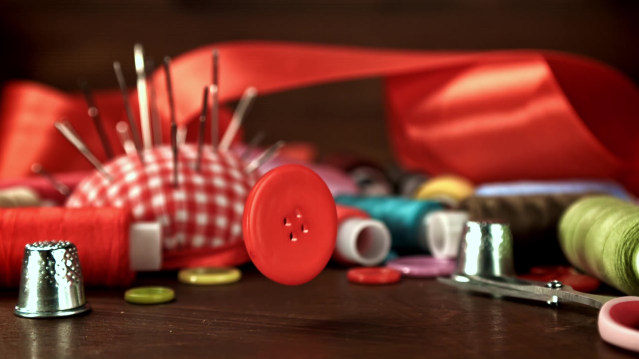 Red Button Falling in Super Slow Motion onto a Wooden Table with Sewing Supplies