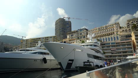 slow revealing shot of super yachts docked in a port with people walking past