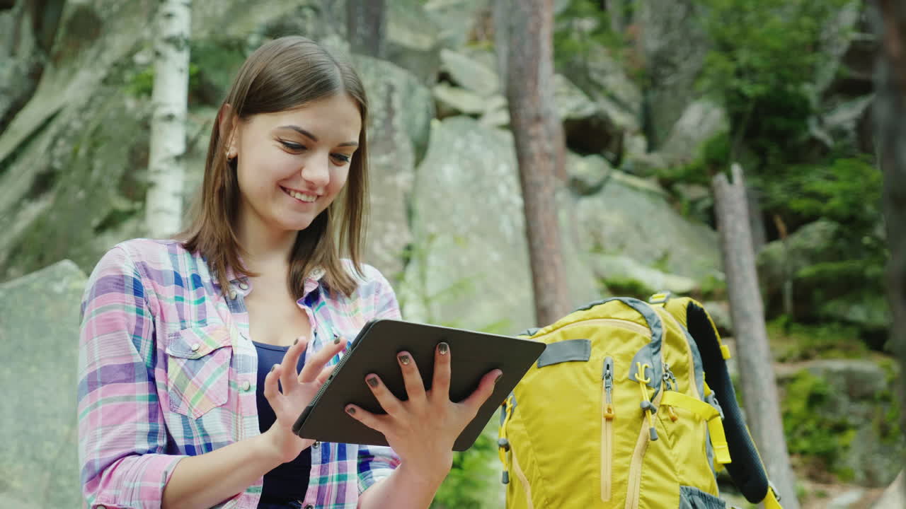 молодая женщина-туристка пользуется смартфоном в походе, сидит, прислонившись к скалам в горах 4k