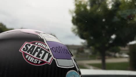 carbon-fiber-hard-hat-sitting-on-the-dashboard-of-a-vehicle-with-a-safety-sticker-and-raindrops-falling-on-the-windshield-wipers