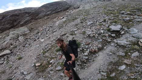 a young, fit man with long hair and a large backpack is jogging and running carefully down a path in themountains full of rocks and stones