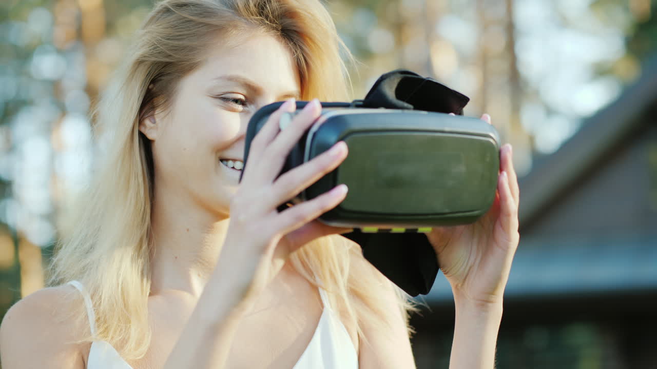 Una bella donna invita nel mondo della realtà virtuale, sorridendo e indossando un casco 3D davanti alla telecamera. 4K.