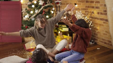 mother and daughters playing having fun laughing, throwing white confetti at home