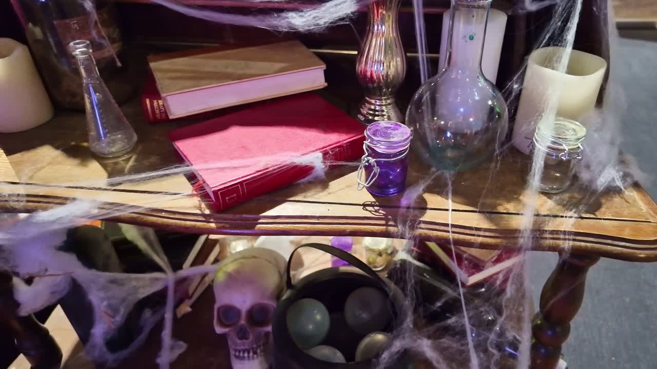 Halloween themed table decorated with cobwebs skulls, candles and potion bottles under direct light