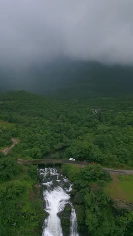 a breathtaking backword drone view of waterfalls in bhandardara, maharashtra, india, surrounded by dense forests and lush green mountains 4k