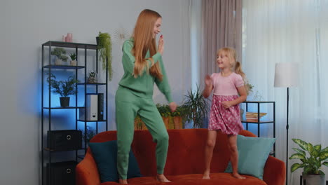 Happy-two-teenage-girls-siblings-best-friends-couple-dancing-at-home-room-on-couch,-disco-party
