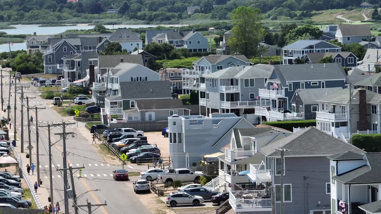 White seagull flying over street of Misquamicut town in Rhode Island. Classical beach houses and homes in town. Aerial wide shot. Cars along street with two-story homes and porch
