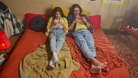 young couple relaxing and gaming on phones in bed