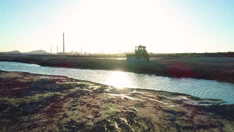 Low-flying-drone-above-toxic-runoff-water-and-asphalt-lake-in-willemstad-curacao,-bulldozer