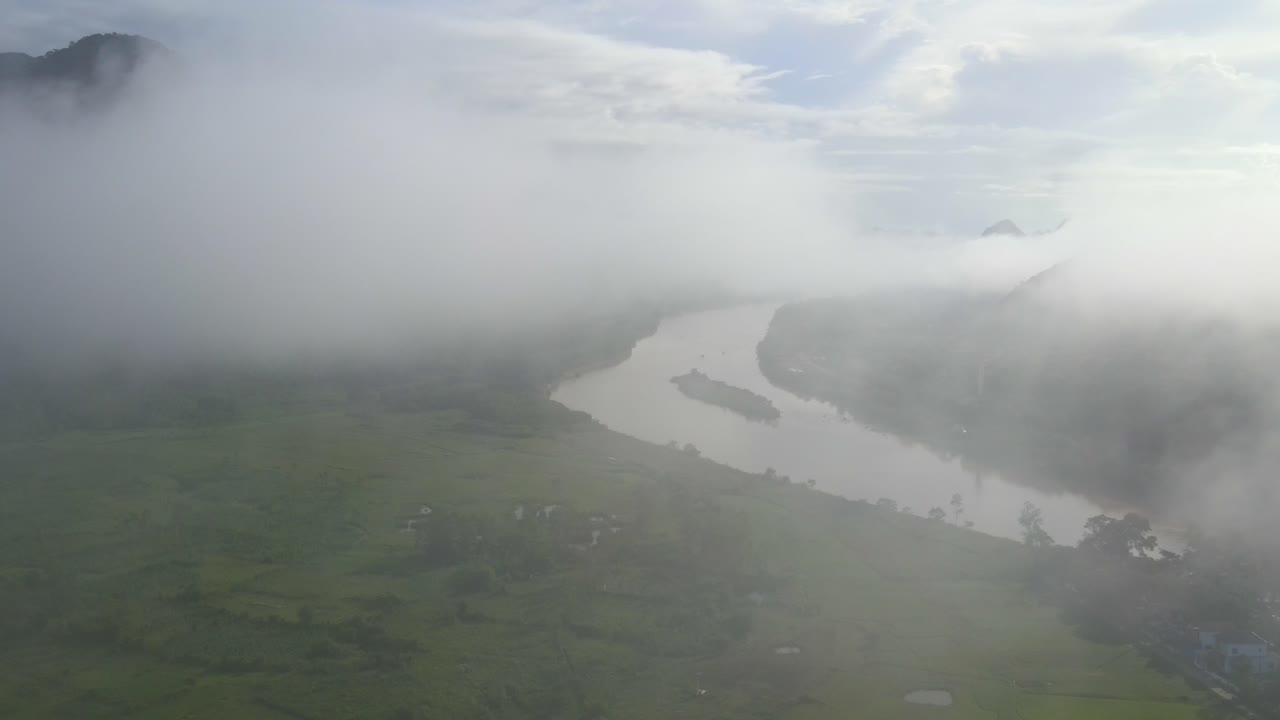 Drone push through the cloud to reveal rice paddies near a windy river