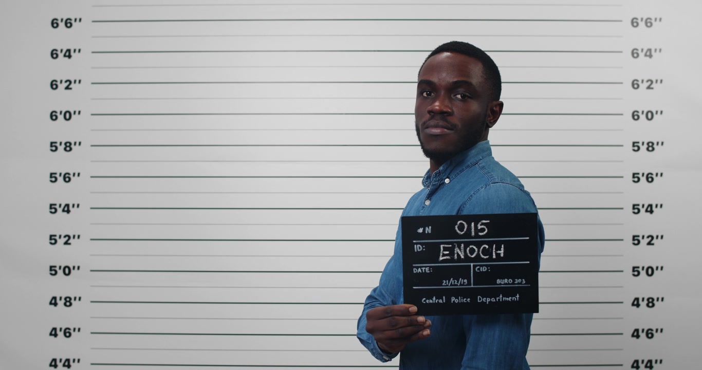 Young Man Holding Mugshot Sign Against Police Lineup Background