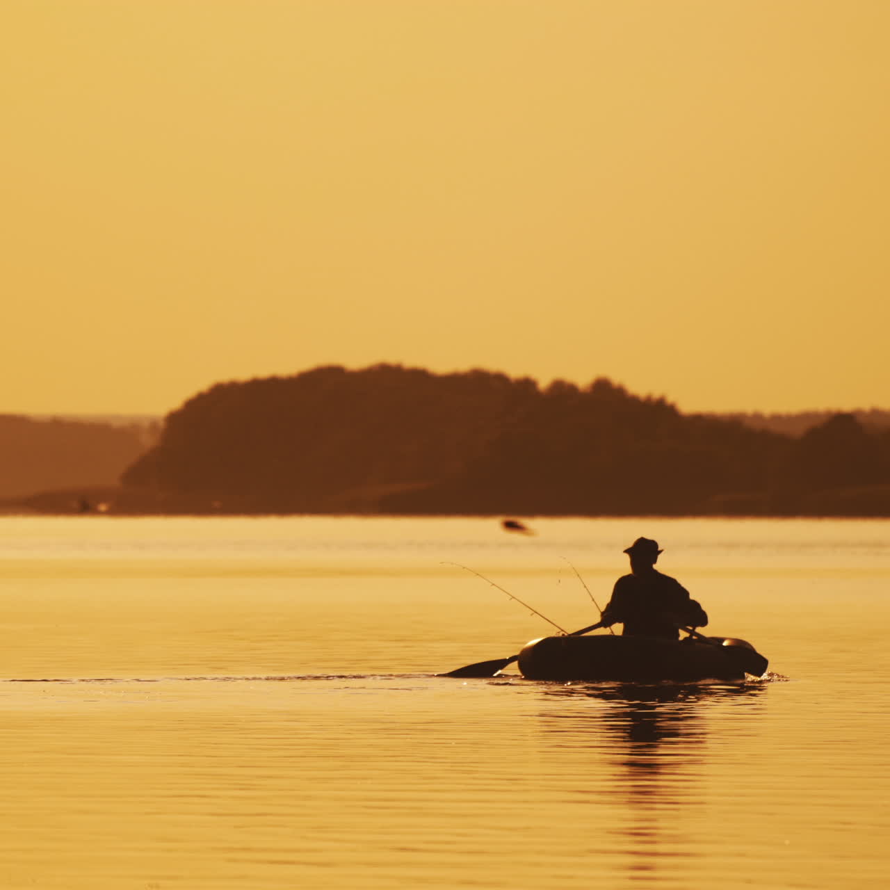 Silhouette of man sailing with two wooden oars on a small boat at sunset time. Beautiful sunset in the river and the silhouette of a man who tries to find a place for fishing on rowboat.