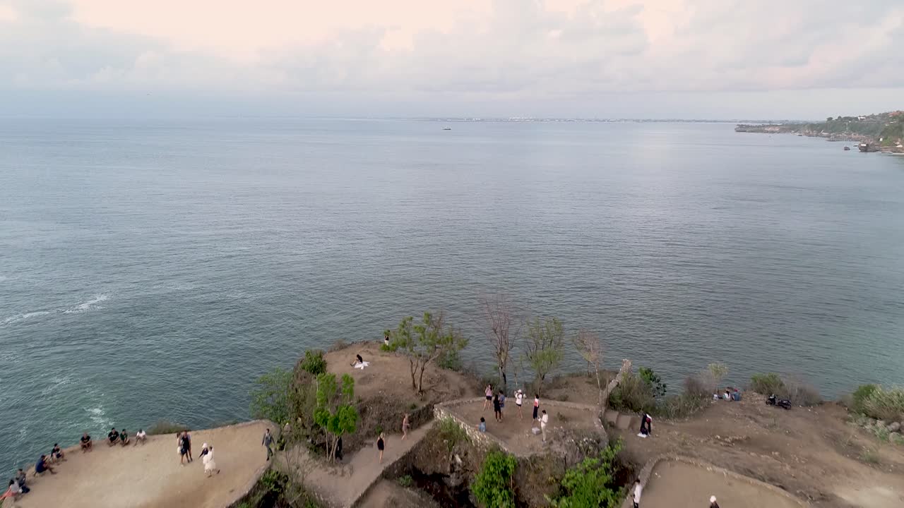 Volo aereo sopra un promontorio roccioso verde con onde e giornata nuvolosa a Balangan Beach, Bali, Indonesia, Asia