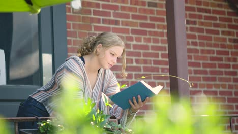 girl reading book outside leaning over a side rail against a brick building