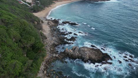 This-drone-video-captures-the-sea-crashing-against-the-rocks-near-Coral-and-Bacocho-beaches-in-Puerto-Escondido,-Oaxaca,-Mexico