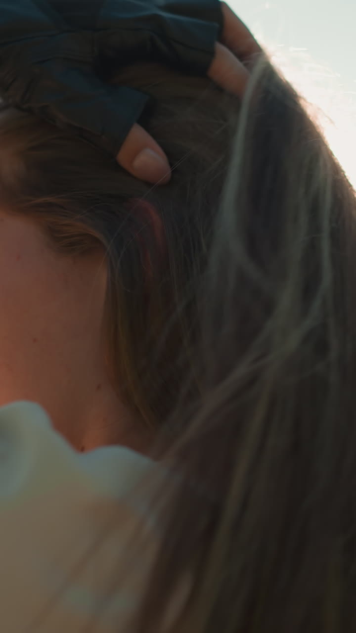 검은 장갑을 입은 여자가 그녀의 긴 머리카락을 우아하게 조정합니다, 부드럽고 따뜻한 빛에 여 그녀의 주변에 자연스러운 빛을 방출합니다, 평온한 배경, 흐릿한 녹색 나무와 잎자루