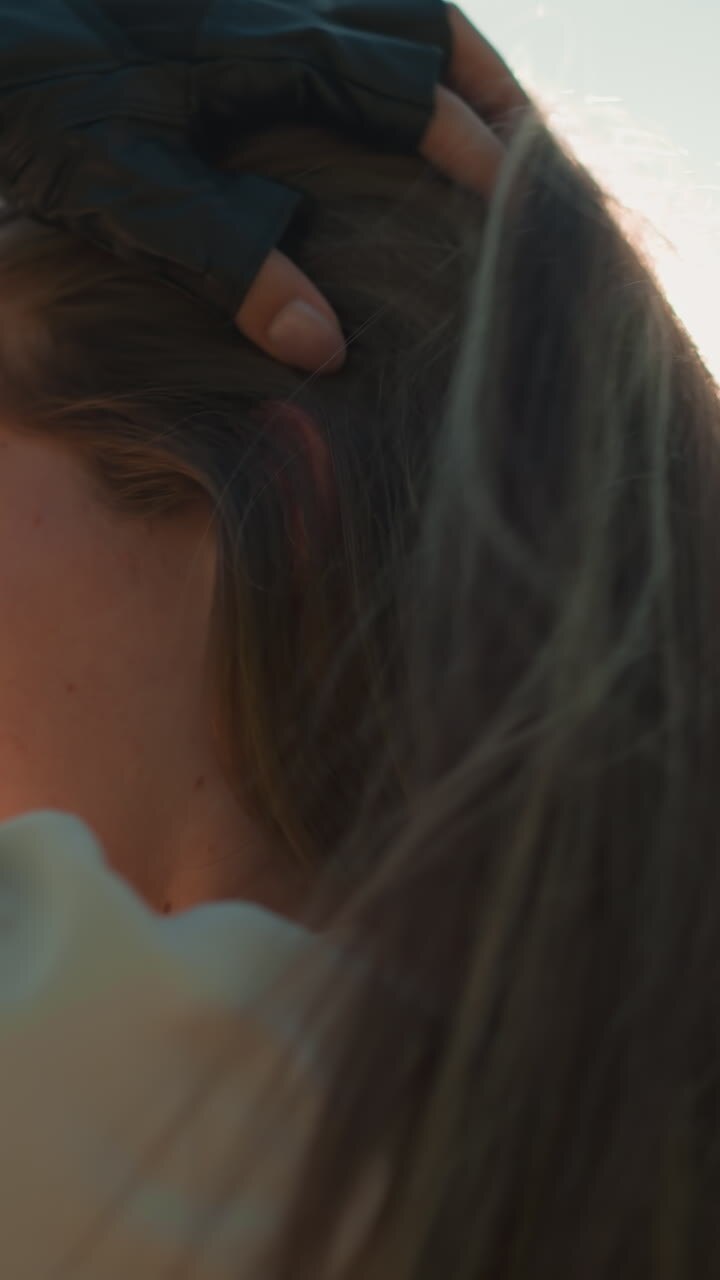 дама в черных перчатках грациозно подстраивает свои длинные волосы, купаясь в мягком, теплом солнечном свете, который бросает естественный блеск вокруг нее, на фоне спокойных, размытых зеленых деревьев и листьев