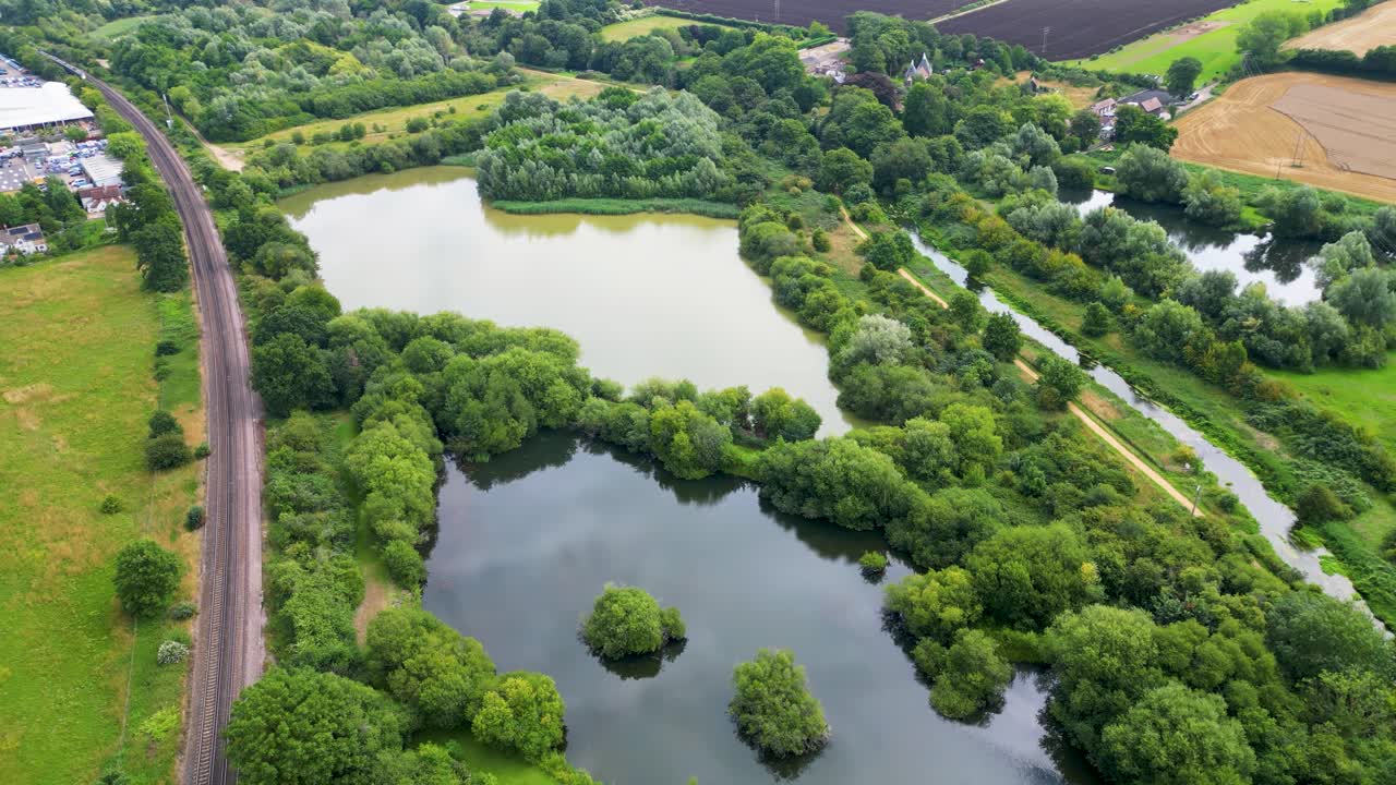 Drone footage passoing over a country road, a train track and then heading off over some lakes
