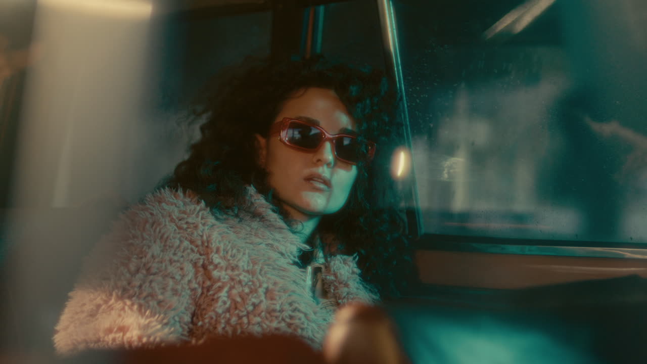 Portrait of Stylish Woman in Sunglasses Sitting in Car Back Seat at Night