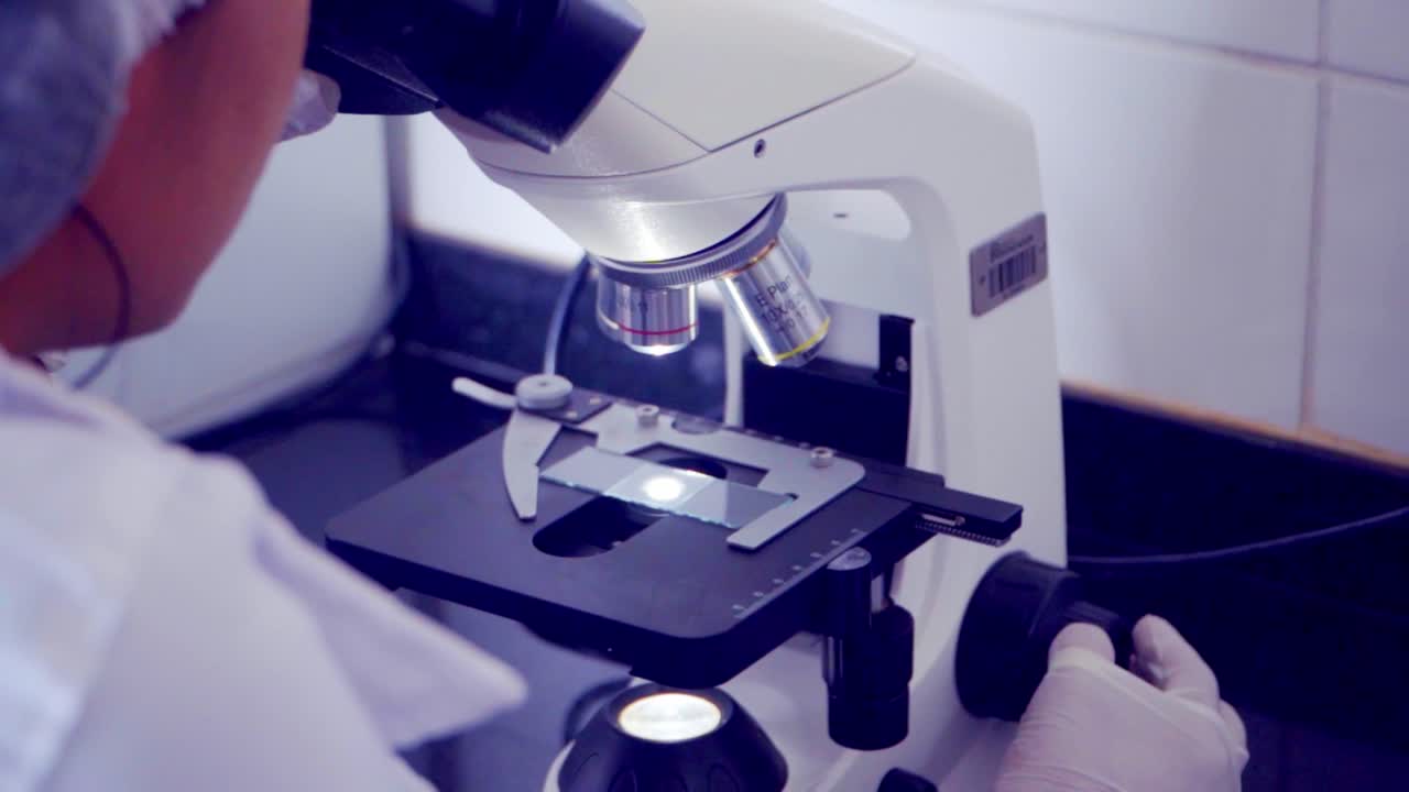 Zoom out revealing research scientist looking at a specimen under a microscope at low magnification