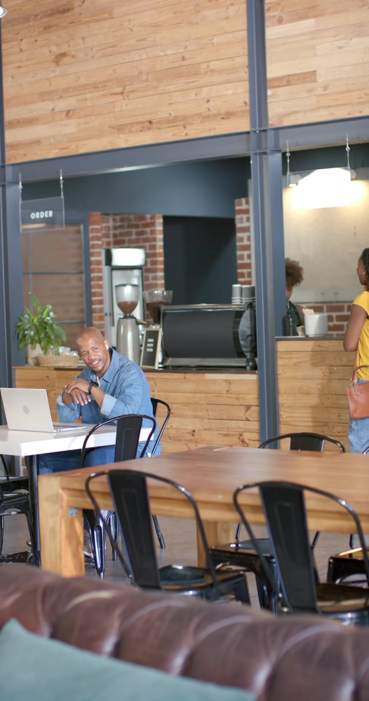 Vertical video: African American woman waiting at counter needing coffee, carrying bag, copy space