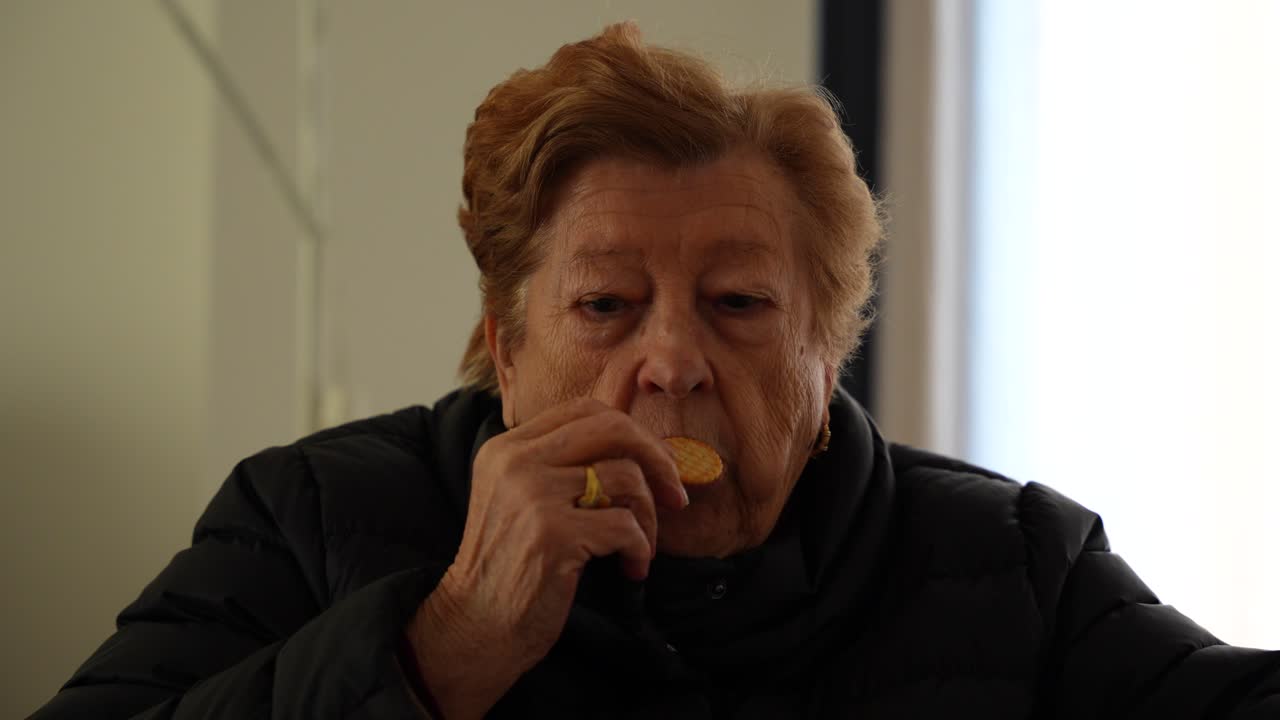 Old woman offering to camera crackers while eats some of them